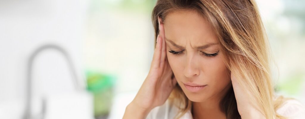Young sad woman suffering from headache pain in kitchen